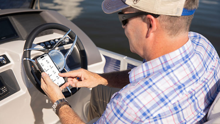 A boat owner sits at the helm of the boat and scrolls the Siren boat app on his phone.