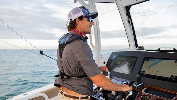 A man wearing a ball cap and sunglasses steering his boat.