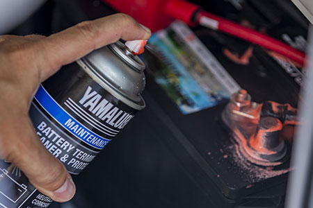 Someone sprays Yamalube Battery Terminal Cleaner & Protector onto a battery.