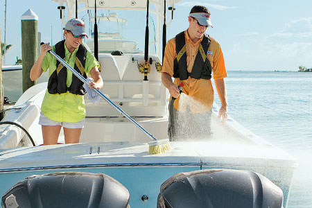 Two boaters cleaning the back of the boat with a broom and water hose.